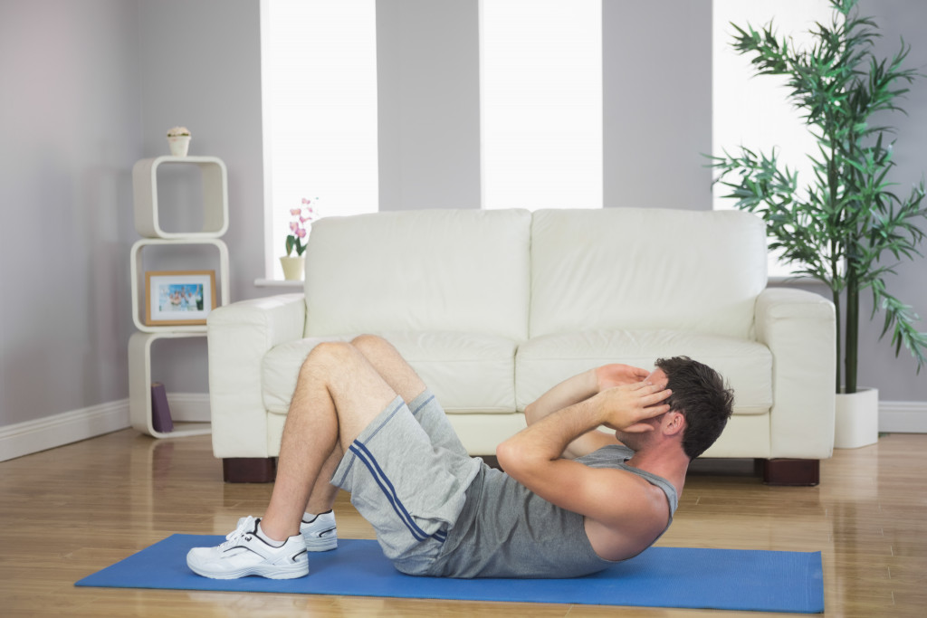 A fit and handsome sporty man doing sit ups in the home living room