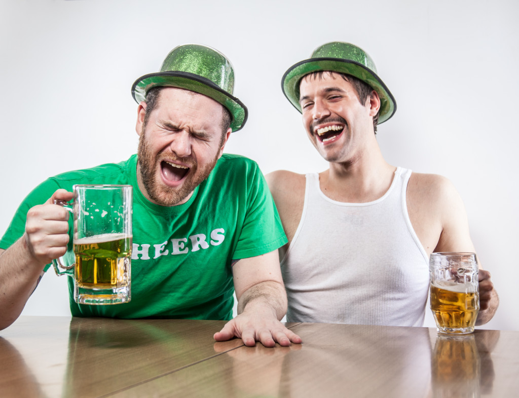 Two men in St. Patrick's day outfits drinking beer while laughing